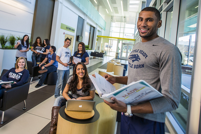 Male student holding a binder with four students standing in the background